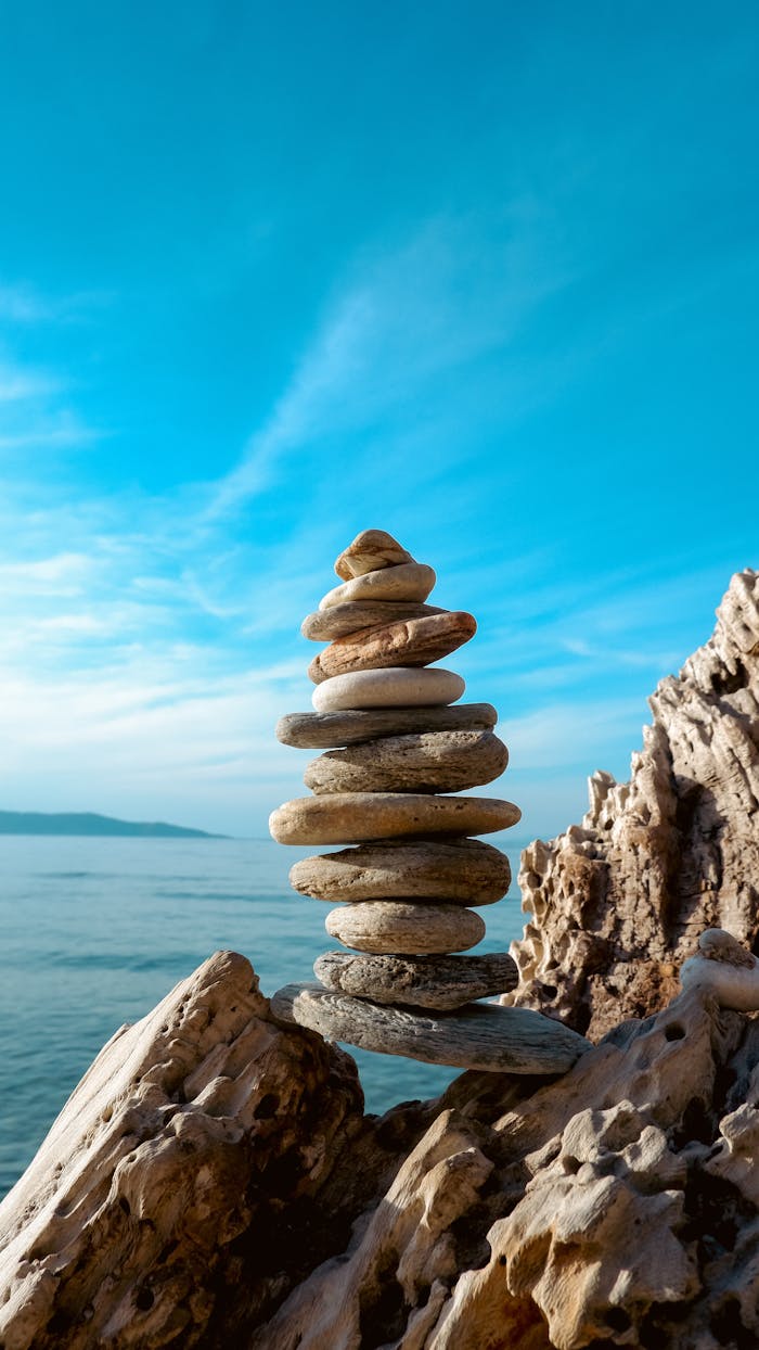 gallery-2 A stack of balanced stones on a rocky seashore with a clear blue sky and sea in the background.