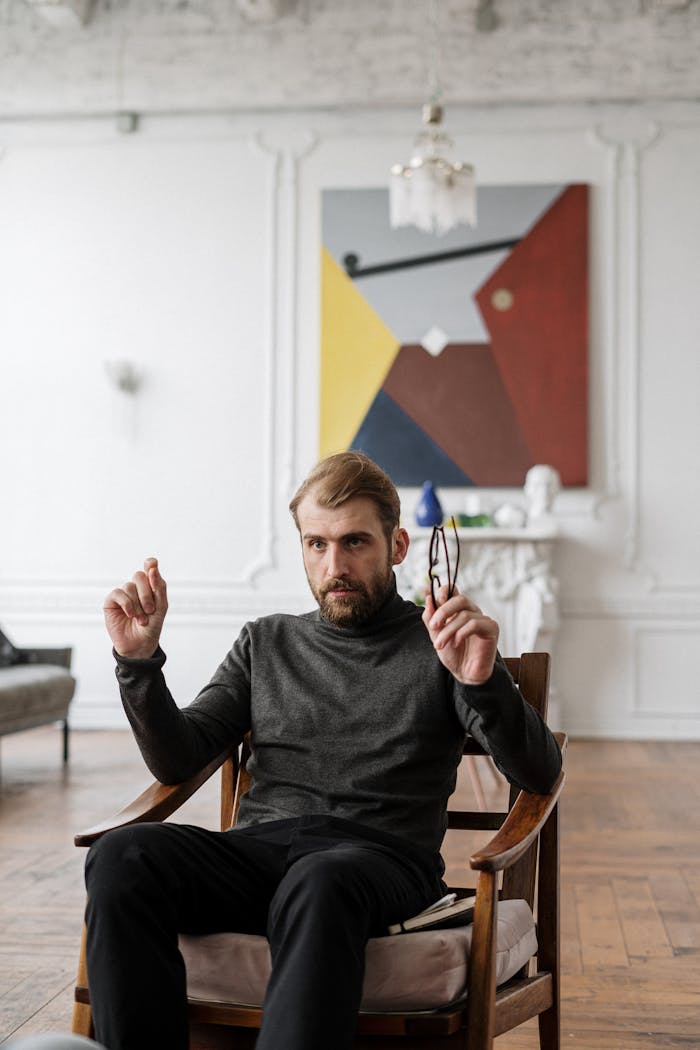A man in a modern interior, sitting in front of an abstract painting, conveying thoughtful expression.