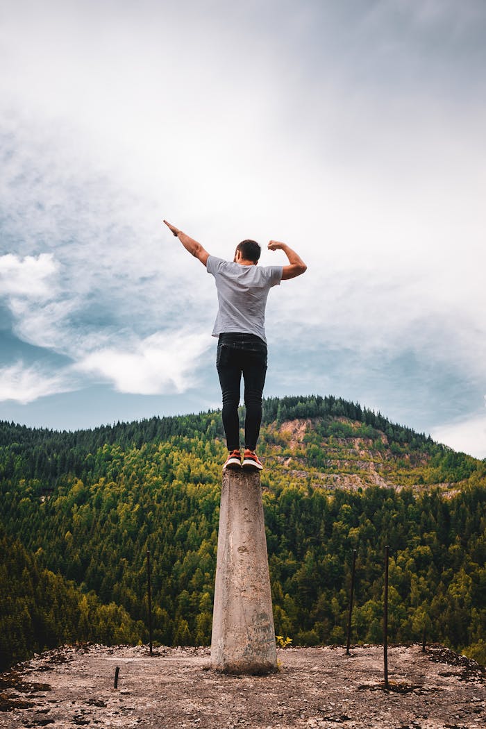 gallery-3 A man standing with raised arms on a pedestal against a mountainscape, showcasing balance and adventure.